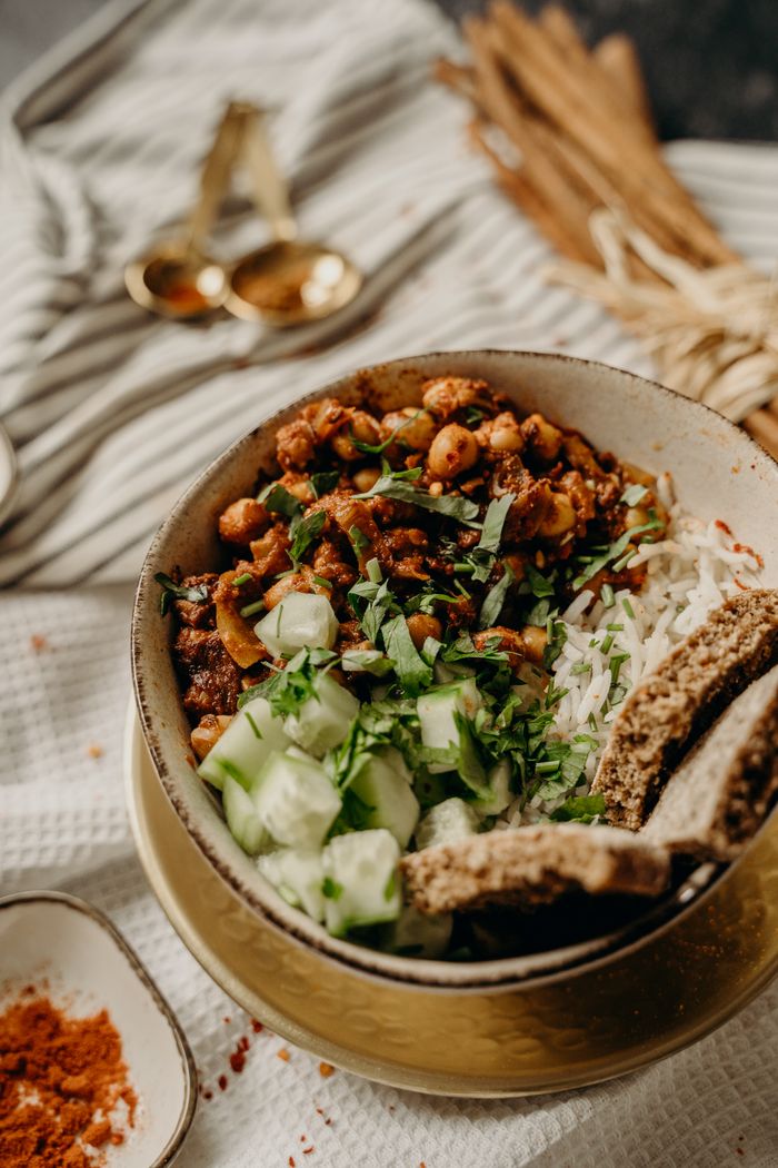 message-img Tasty vegan bowl with chickpeas, rice, cucumber, and herbs on a rustic table.