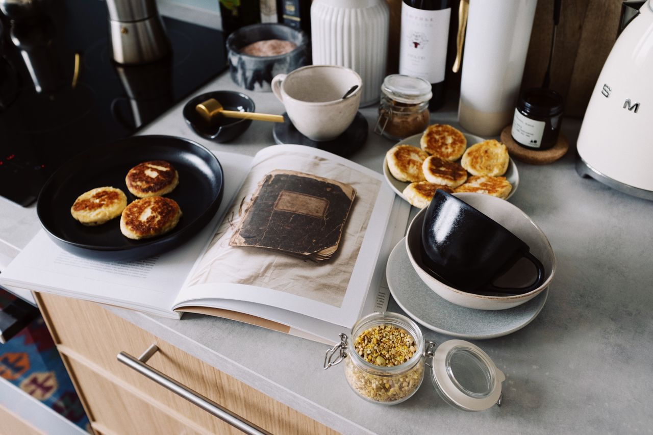 our-history-img High angle of cookbook and cooked fritters on plates placed on table near utensils and ingredients in cozy kitchen at home